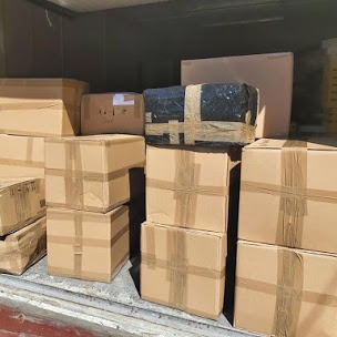 Kartonowe pudła różnej wielkości, zabezpieczone taśmą, ułożone w stos wewnątrz pojazdu, prawdopodobnie przed lub po transporcie.