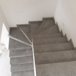 Zakład instalacyjno budowlany Roman Kozak - Wykończone schody z szarej płytki, widok z góry. Detal wykończenia krawędzi. Minimalistyczny design, surowe wnętrze w trakcie prac wykończeniowych.