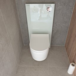 Zakład instalacyjno budowlany Roman Kozak - Nowoczesna toaleta podwieszana z białym panelem i szarą glazurą w wykończonej łazience w Czempiniu. Widok z góry, minimalistyczny design.