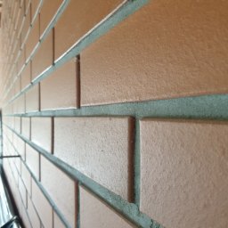 Zakład instalacyjno budowlany Roman Kozak - Ceglana ściana z szarą fugą, ułożona pod kątem, z widoczną fakturą cegieł i spoin. Perspektywa podkreśla głębię i regularność wzoru. Częściowo widoczne elementy konstrukcji.