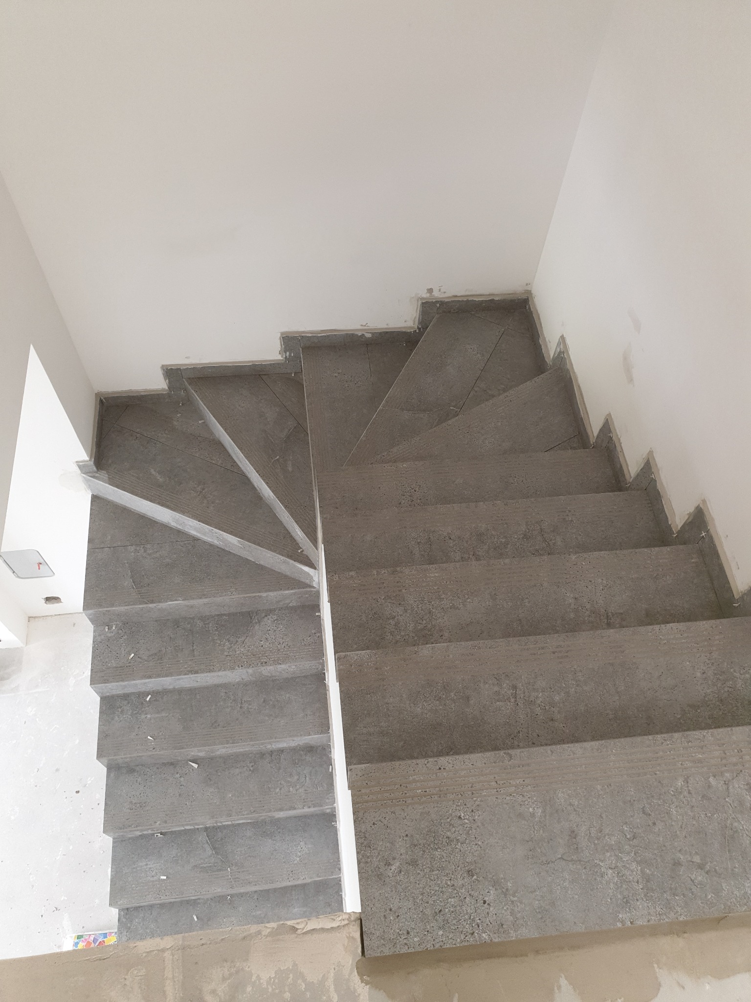 Wykończone schody z szarej płytki, widok z góry. Detal wykończenia krawędzi. Minimalistyczny design, surowe wnętrze w trakcie prac wykończeniowych.