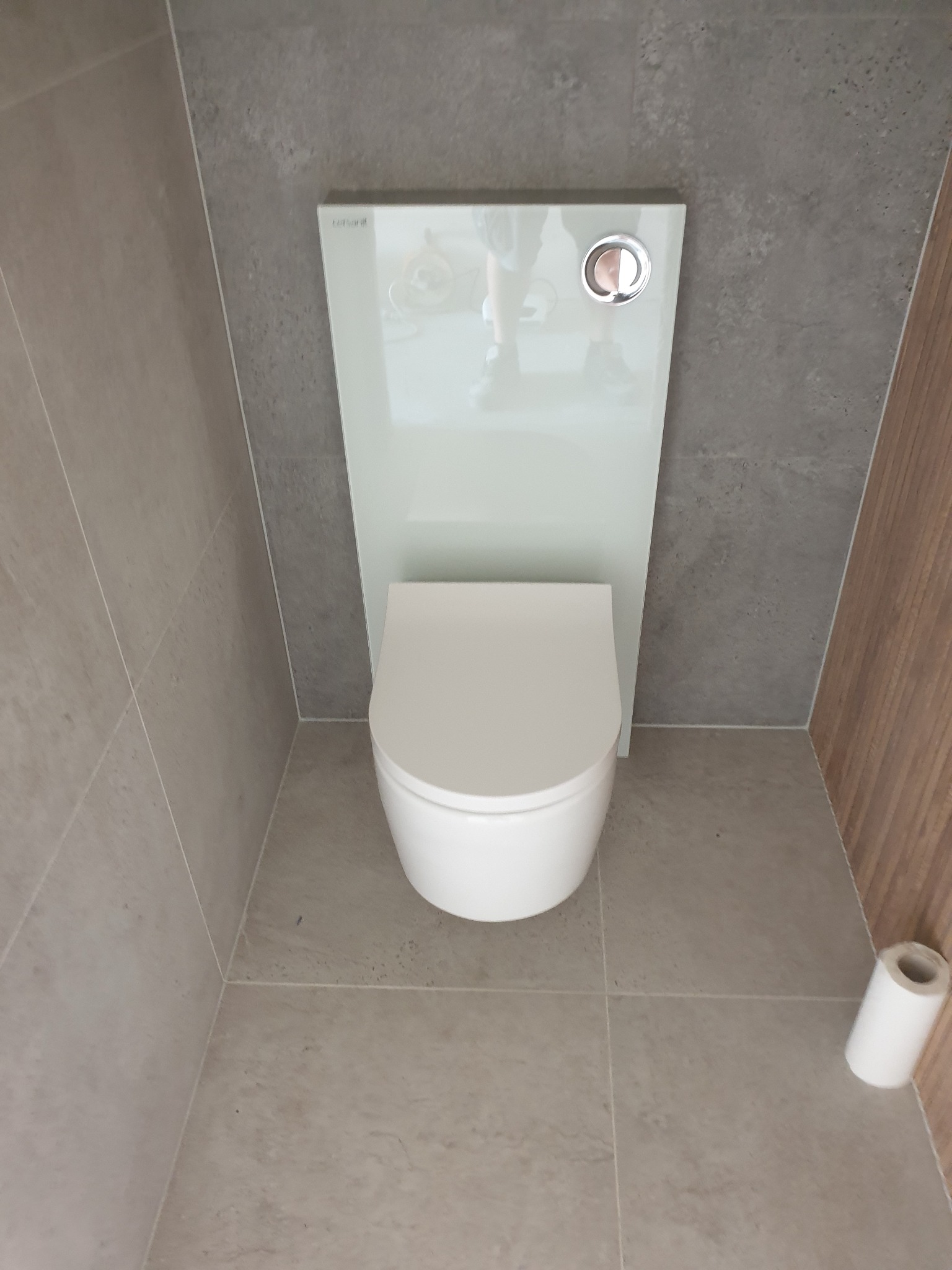 Nowoczesna toaleta podwieszana z białym panelem i szarą glazurą w wykończonej łazience w Czempiniu. Widok z góry, minimalistyczny design.