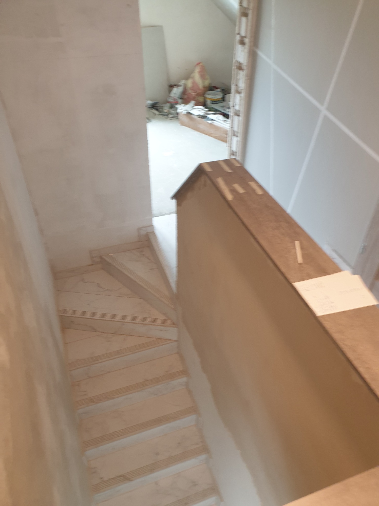 Wykończenie schodów marmurowych w jasnym wnętrzu. Widoczne płyty karton-gips na ścianach i elementy konstrukcyjne. Ujęcie z góry, podkreślające detale wykończenia.