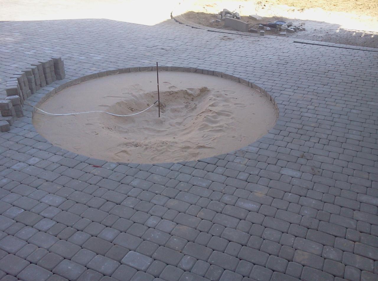 Układanie kostki brukowej w Wasilkowie: Okrągły wzór z piaskiem w centrum, otoczony szarą kostką. Częściowo ułożona kostka podkreśla precyzję wykonania.