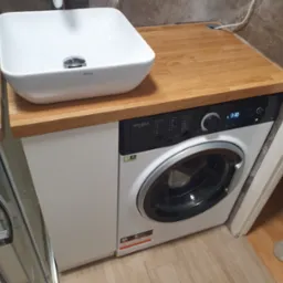Łazienka po remoncie: umywalka nablatowa Ravak na drewnianym blacie nad pralką Whirlpool, widoczna kabina prysznicowa.