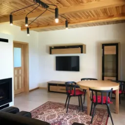 Jasne wnętrze z drewnianym sufitem, okrągłym stołem z czarnymi krzesłami z czerwonymi poduszkami, kominkiem i orientalnym dywanem.