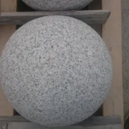 Szare kule z granitu na drewnianej palecie. Element dekoracyjny ogrodu. Widoczny fragment buta w prawym dolnym rogu.