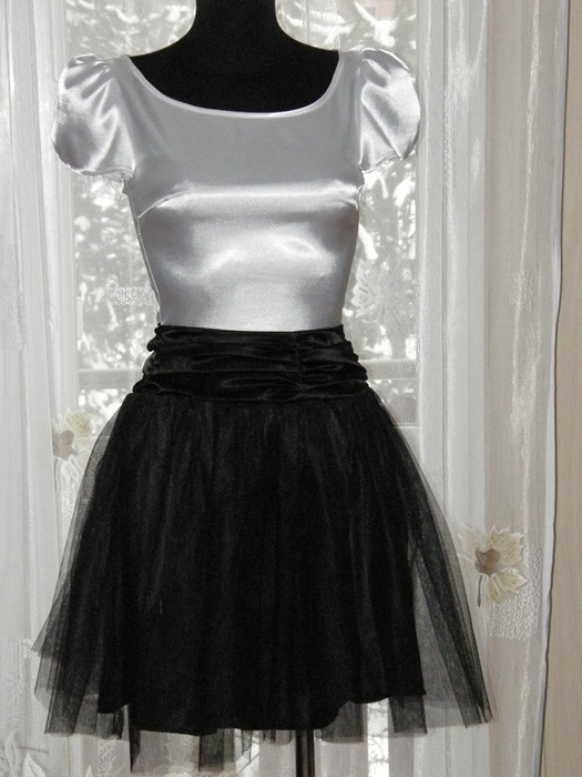 Manekin prezentuje biało-czarną sukienkę z satynową górą i tiulowym dołem na tle okna z białymi zasłonami.