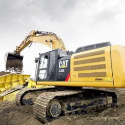 Żółta hybrydowa koparka CAT 336E w trakcie załadunku urobku do przesiewacza na nierównym terenie.