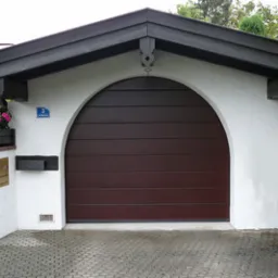 Garaż z brązową bramą segmentową w kształcie łuku, białe ściany z dekoracyjnymi drewnianymi elementami, skrzynka na listy i donica z kwiatami.