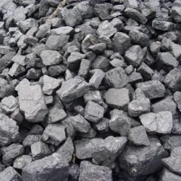 Kupa antracytu o nieregularnych kształtach, z widocznymi błyszczącymi powierzchniami i drobnymi okruchami, oświetlona naturalnym światłem.