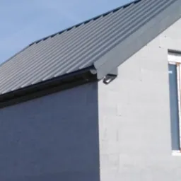 Szary dach z blachy trapezowej na nowoczesnym domu z betonu komórkowego, widoczny fragment okna i rynna.