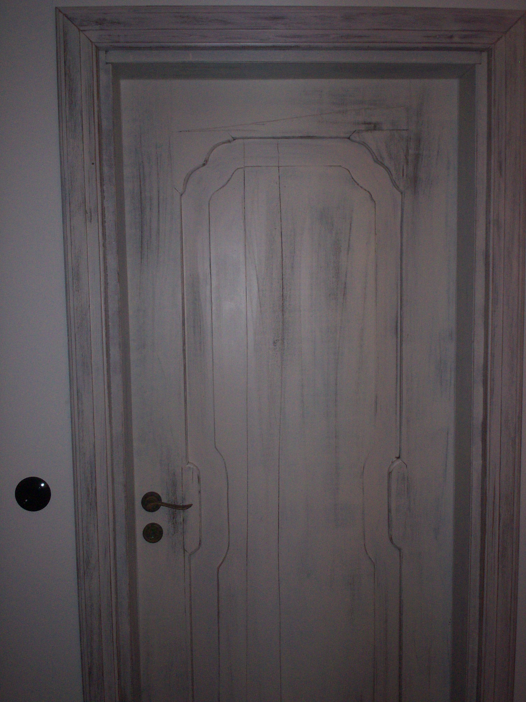 Drzwi drewniane w stylu vintage, pomalowane na biało z efektem postarzenia, z ozdobnym frezowaniem i mosiężną klamką.