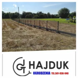 Długie ogrodzenie panelowe z podmurówką betonową na polu po żniwach, widok z perspektywy bocznej, w tle drzewa i niebieskie niebo, w dolnej części logo firmy.
