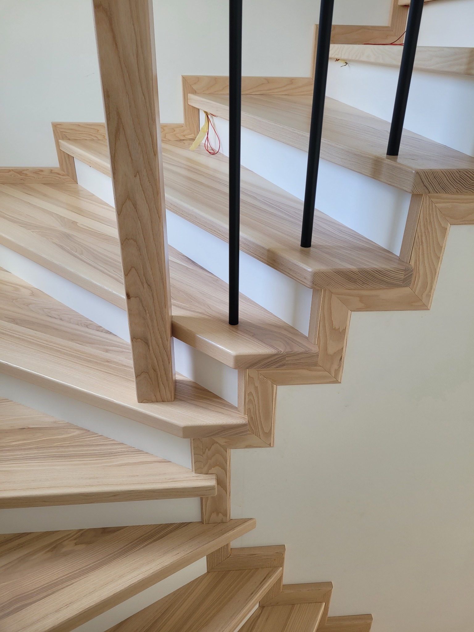 Jasne, drewniane schody z czarnymi, metalowymi balustradami, widoczne z dołu, z detalami wykończenia i teksturą drewna.