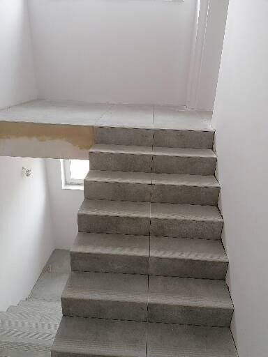 Surowe, betonowe schody w trakcie budowy lub remontu, widoczne niedokończone ściany i podesty, surowy stan wykończenia.