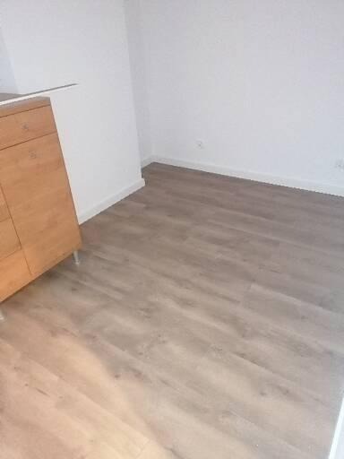 Jasne panele podłogowe ułożone w nowym mieszkaniu, widoczne od strony szafki z jasnego drewna i białych ścian.