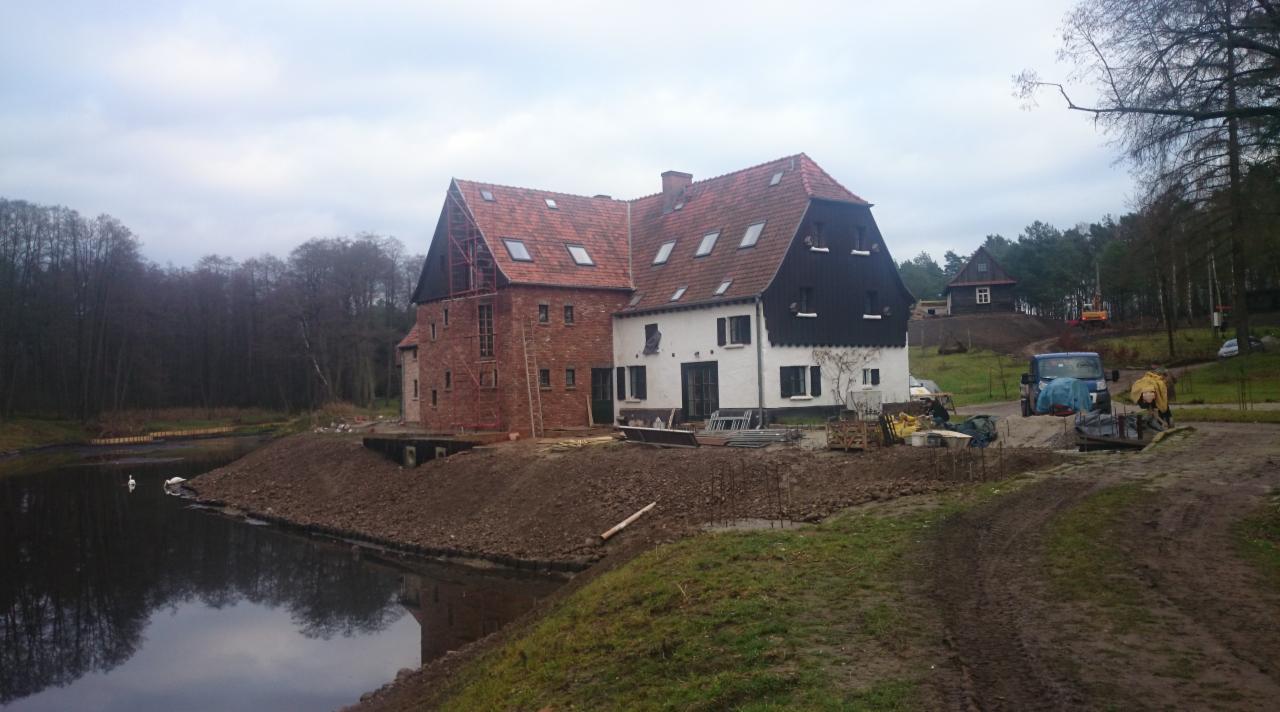 Rozbudowa dwukondygnacyjnego domu z cegły i białego tynku z ciemnymi elementami, widok na elewację i dach z czerwonej dachówki, jezioro w tle.
