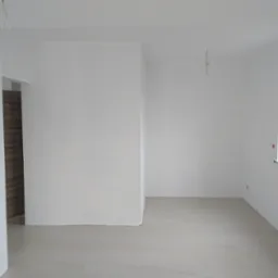 Wnętrze świeżo pomalowanego na biało pomieszczenia z widocznymi puszkami farby w tle, schodami i oknem, ukazujące efekt gładkich ścian i jasnej przestrzeni.