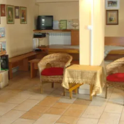 Przytulne wnętrze pokoju z kominkiem, wiklinowymi fotelami z czerwonymi poduszkami i drewnianymi ławami, udekorowane obrazami na ścianach.