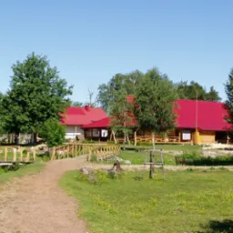 Drewniane budynki z czerwonymi dachami w otoczeniu zieleni, połączone drewnianymi mostkami, tworzące kompleks wypoczynkowy.