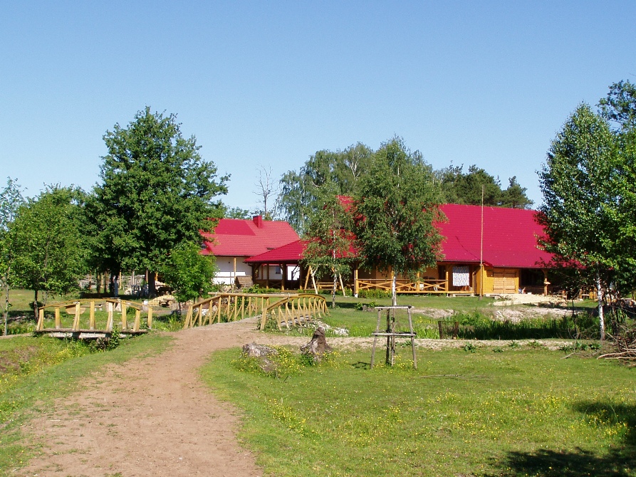 Drewniane budynki z czerwonymi dachami w otoczeniu zieleni, połączone drewnianymi mostkami, tworzące kompleks wypoczynkowy.