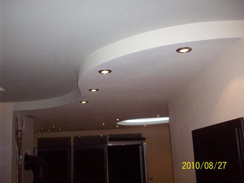 Wykończony sufit podwieszany z zaokrąglonymi krawędziami i wbudowanymi punktowymi lampami halogenowymi, widok z dołu w kierunku otwartego pomieszczenia.