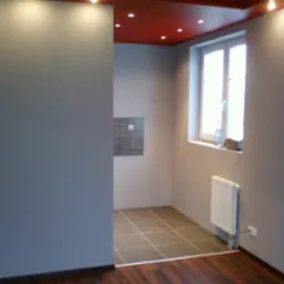 Wykończone wnętrze: szare ściany, drewniana podłoga przechodząca w kafelki w łazience, czerwony sufit z oświetleniem punktowym oraz biały grzejnik pod oknem.