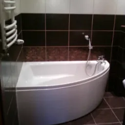 Nowoczesna, narożna wanna w wykończonej łazience z brązowymi i białymi płytkami oraz grzejnikiem drabinkowym.