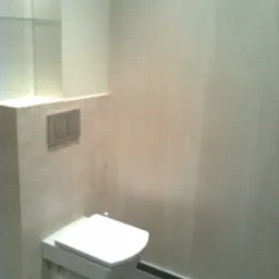 Wisząca toaleta z zabudowaną spłuczką na tle beżowych płytek i szarej podłogi z ciemną listwą przypodłogową, w łazience wykończonej w odcieniach beżu i szarości.