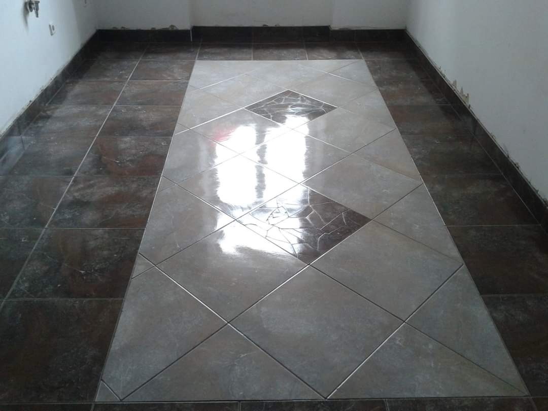 Ułożona podłoga z płytek w dwóch odcieniach szarości z ciemniejszą obwódką i centralnym wzorem w kształcie rombu, widoczne niedoskonałości przy ścianach.