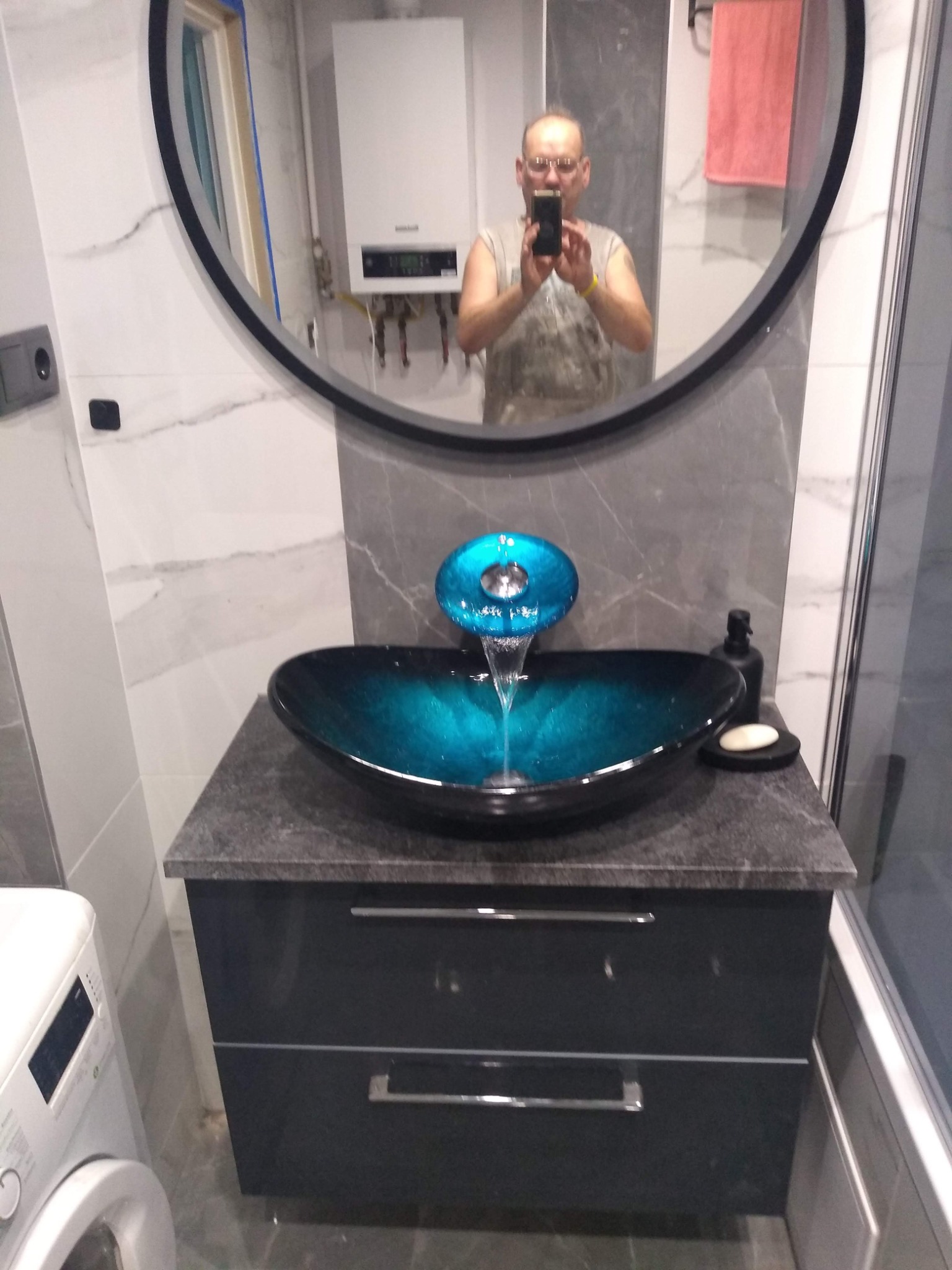 Nowoczesna łazienka z umywalką w kolorze turkusowym, armaturą z wodospadem i odbiciem fotografa w lustrze.