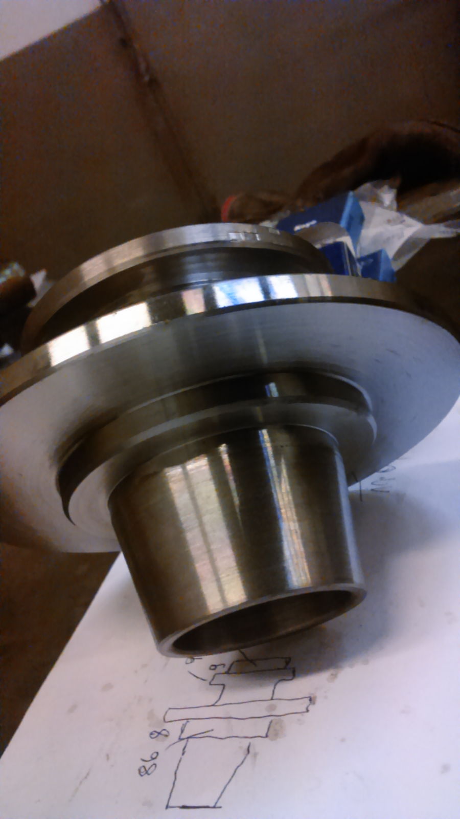 Metalowy element z rysunkiem technicznym, wykonany prawdopodobnie na tokarce. Widoczne ślady obróbki skrawaniem i wysoki połysk.