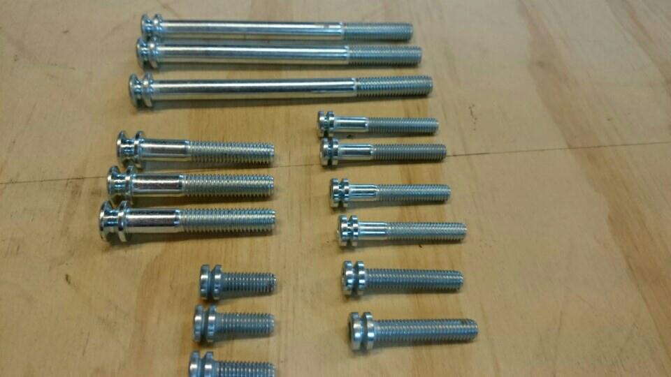 Precyzyjnie wykonane, gwintowane śruby o różnych długościach, ułożone na drewnianej powierzchni. Widoczne detale gwintu i metaliczny połysk.