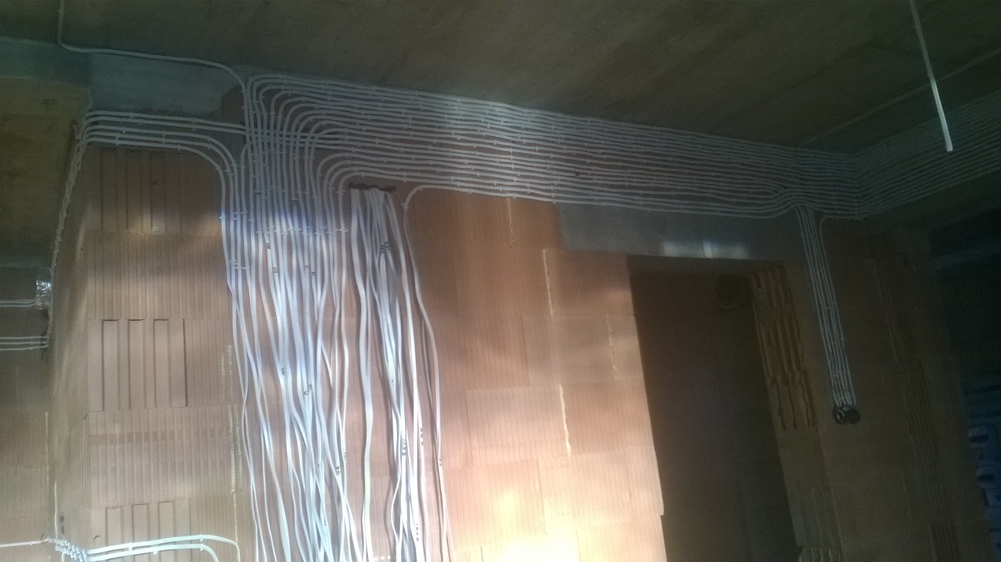 Układ białych kabli elektrycznych przymocowanych do surowej ceglanej ściany w nowo budowanym domu, widok z dołu.