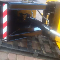 Detail of a new, black snow plow attachment with red and white safety stripes, hydraulic cylinder visible, resting on a wooden pallet.