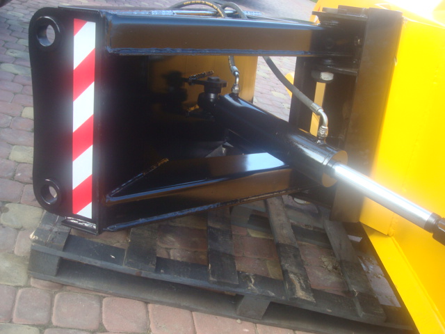 Detail of a new, black snow plow attachment with red and white safety stripes, hydraulic cylinder visible, resting on a wooden pallet.