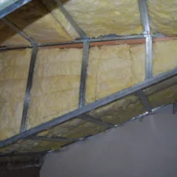 Ocieplenie poddasza wełną mineralną, widoczne metalowe profile konstrukcyjne, surowy stan przed zabudową płytami gipsowo-kartonowymi.