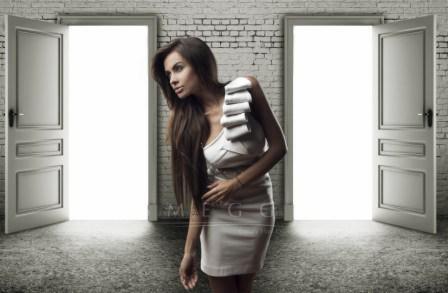 Kobieta z długimi brązowymi włosami, w białej sukience, z ręcznikami na ramieniu, stoi pomiędzy dwoma otwartymi drzwiami w ceglanej ścianie.