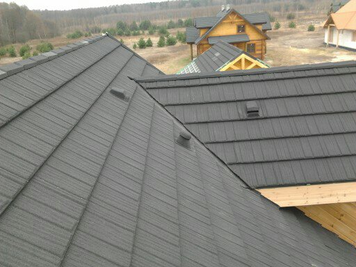Ciemnoszara dachówka modułowa na ukończonym dachu nowego domu z drewnianą konstrukcją w tle, widoczne kominki wentylacyjne.