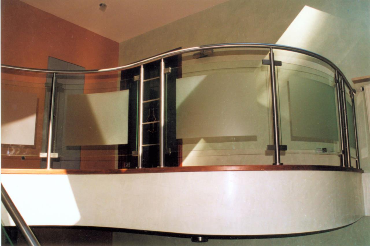 Nierdzewna balustrada wewnętrzna z giętym szkłem, widoczna na półpiętrze, z elementami drewnianymi i oświetleniem punktowym.