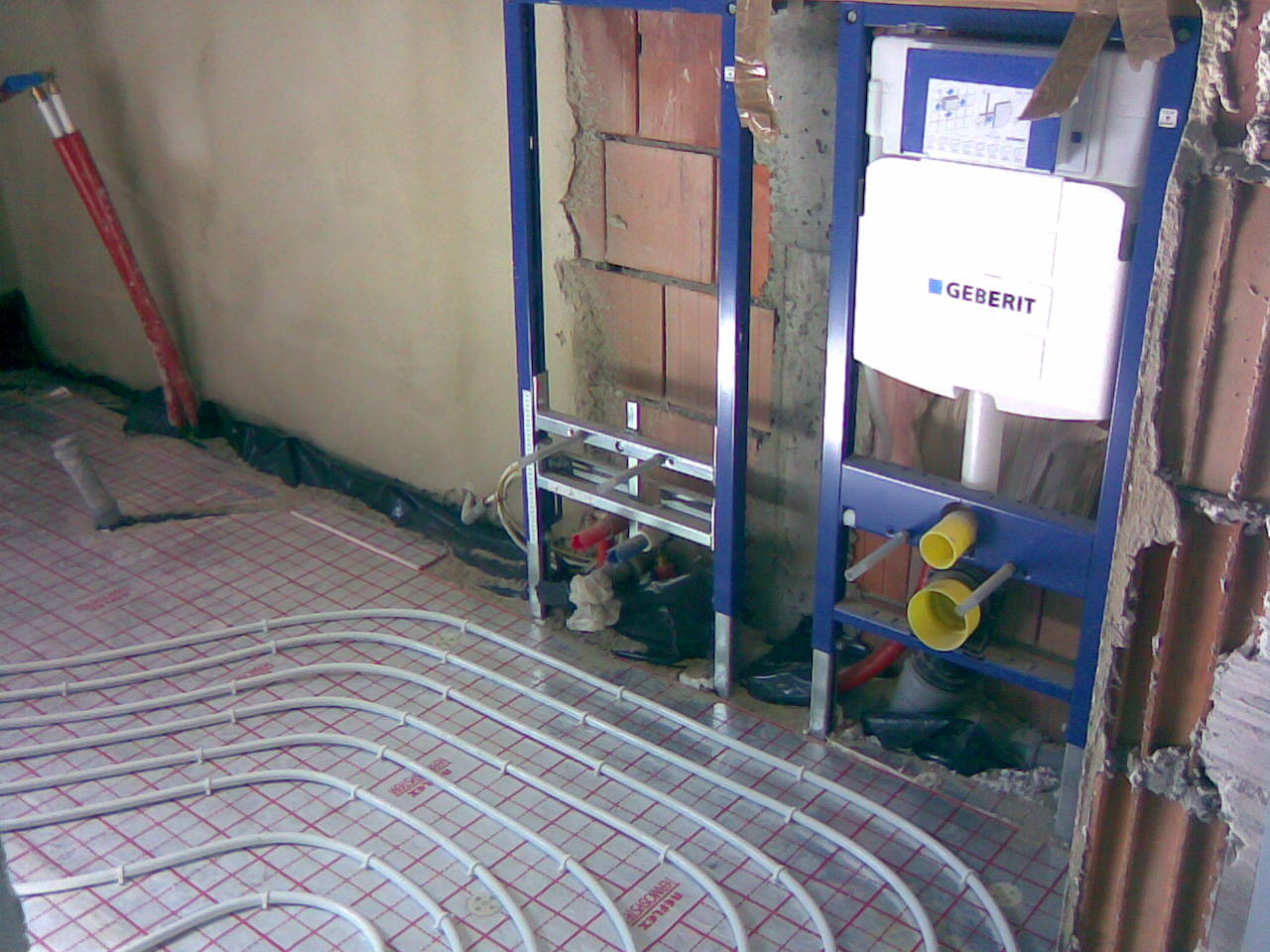 Montaż podtynkowego stelaża WC Geberit z widoczną instalacją ogrzewania podłogowego w trakcie prac wykończeniowych.