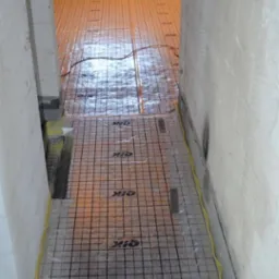 Przygotowanie podłoża pod posadzkę: folia z siatką i logo OIK rozłożona na podłodze, ściany z surowego betonu, żółta taśma zabezpieczająca przy ścianach.