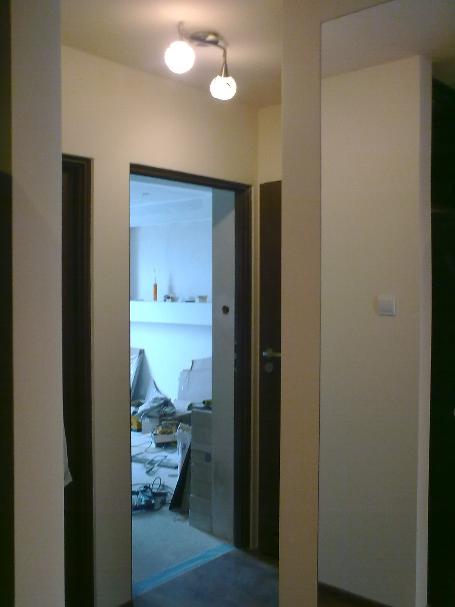 Korytarz w trakcie prac wykończeniowych, widoczne narzędzia, zakryte folią sprzęty i świeżo pomalowane ściany w odcieniach beżu i bieli.