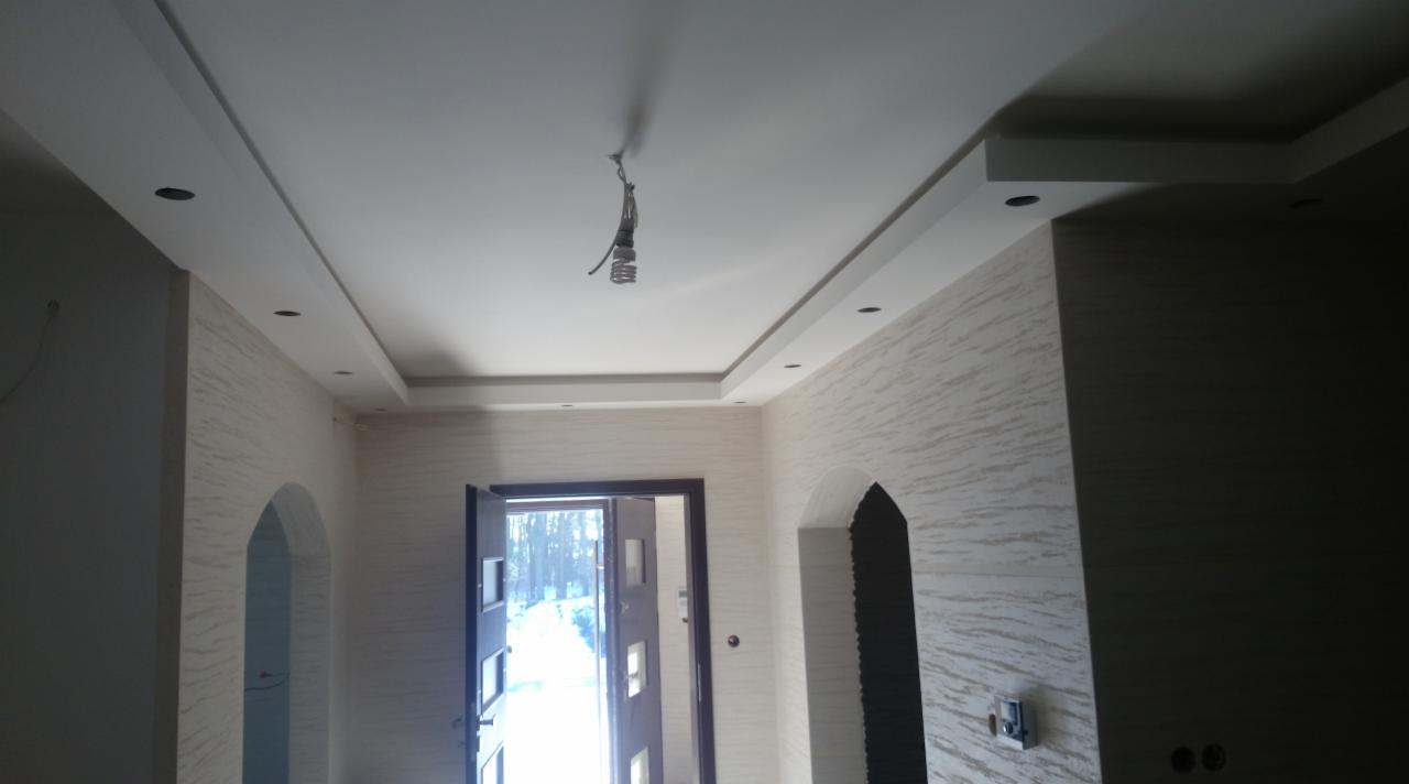 Wykończone wnętrze korytarza z dekoracyjnymi ścianami w odcieniach beżu, podwieszanym sufitem z oświetleniem punktowym i otwartymi drzwiami wejściowymi.