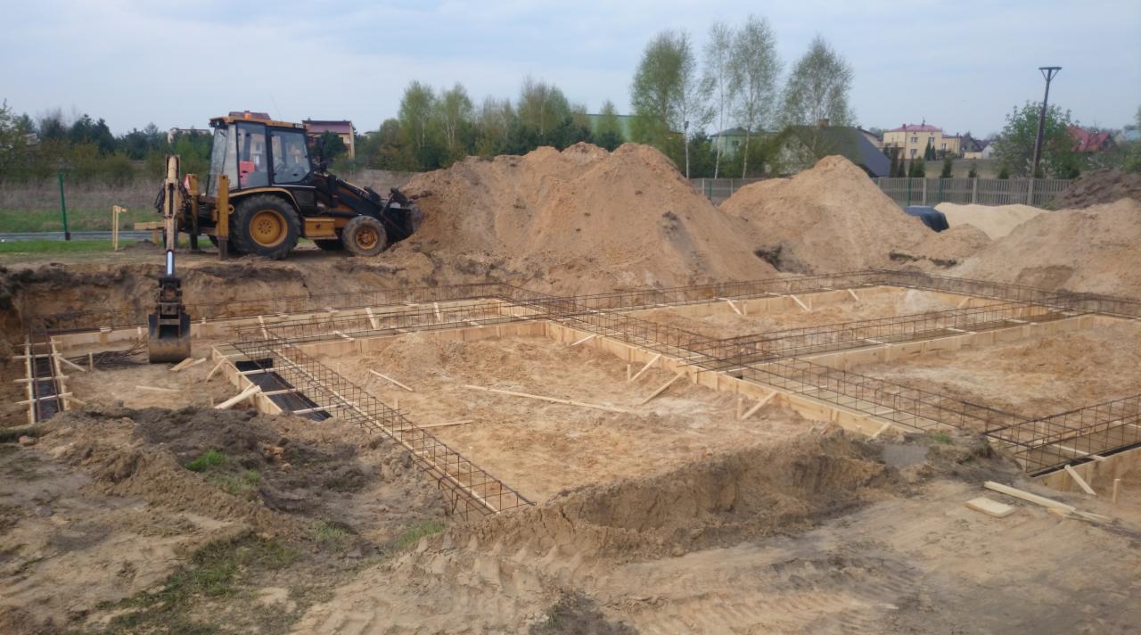 Wykop pod fundamenty domu zbrojony stalą i deskowaniem. Na górze koparka i hałda ziemi. Początek budowy domu.