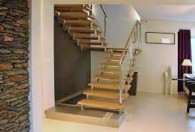 Nowoczesne schody drewniano-metalowe w Płocku. Stopnie z jasnego drewna, metalowa barierka. Ściana z kamienia dekoracyjnego, minimalistyczny design.