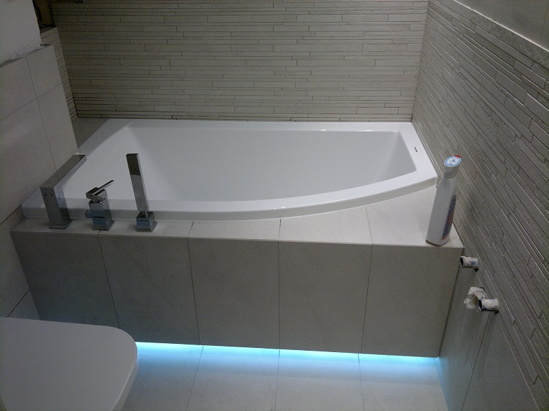 Biała wanna obudowana płytkami z nowoczesną armaturą i podświetleniem LED od dołu, widoczna butelka środka czyszczącego na obudowie wanny.