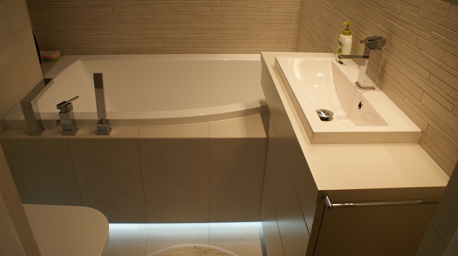 Nowoczesna łazienka z białą wanną, umywalką nablatową i chromowanymi bateriami w minimalistycznym stylu, podświetlenie LED pod wanną.