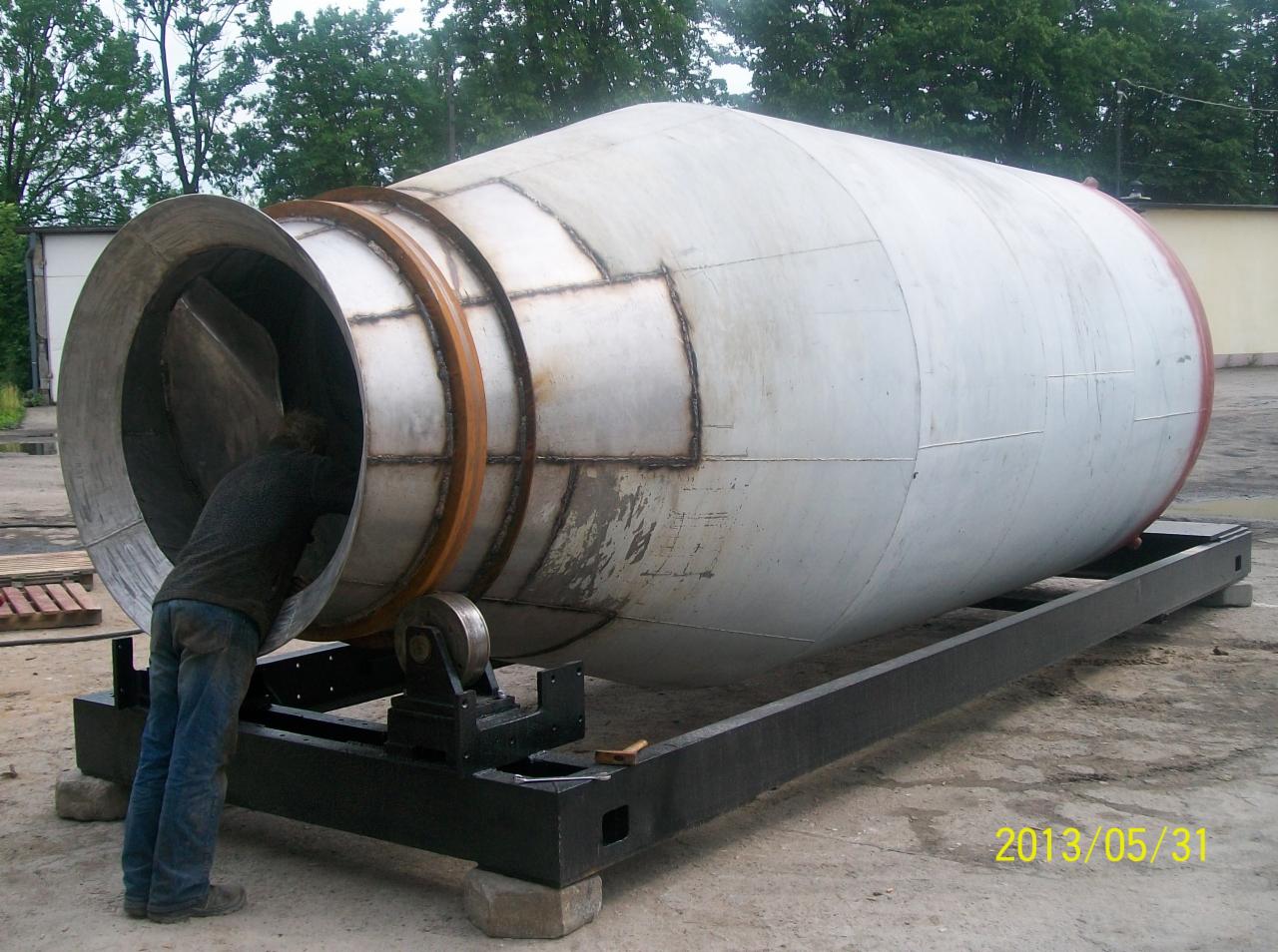 Spawana, metalowa konstrukcja przypominająca bęben betoniarki, umieszczona na czarnej, stalowej ramie. Mężczyzna pochylony wewnątrz cylindra. Widoczna data 2013/05/31.